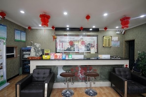 Un espace d’accueil comprenant un comptoir, deux tabourets de bar et un coin salon avec deux chaises.