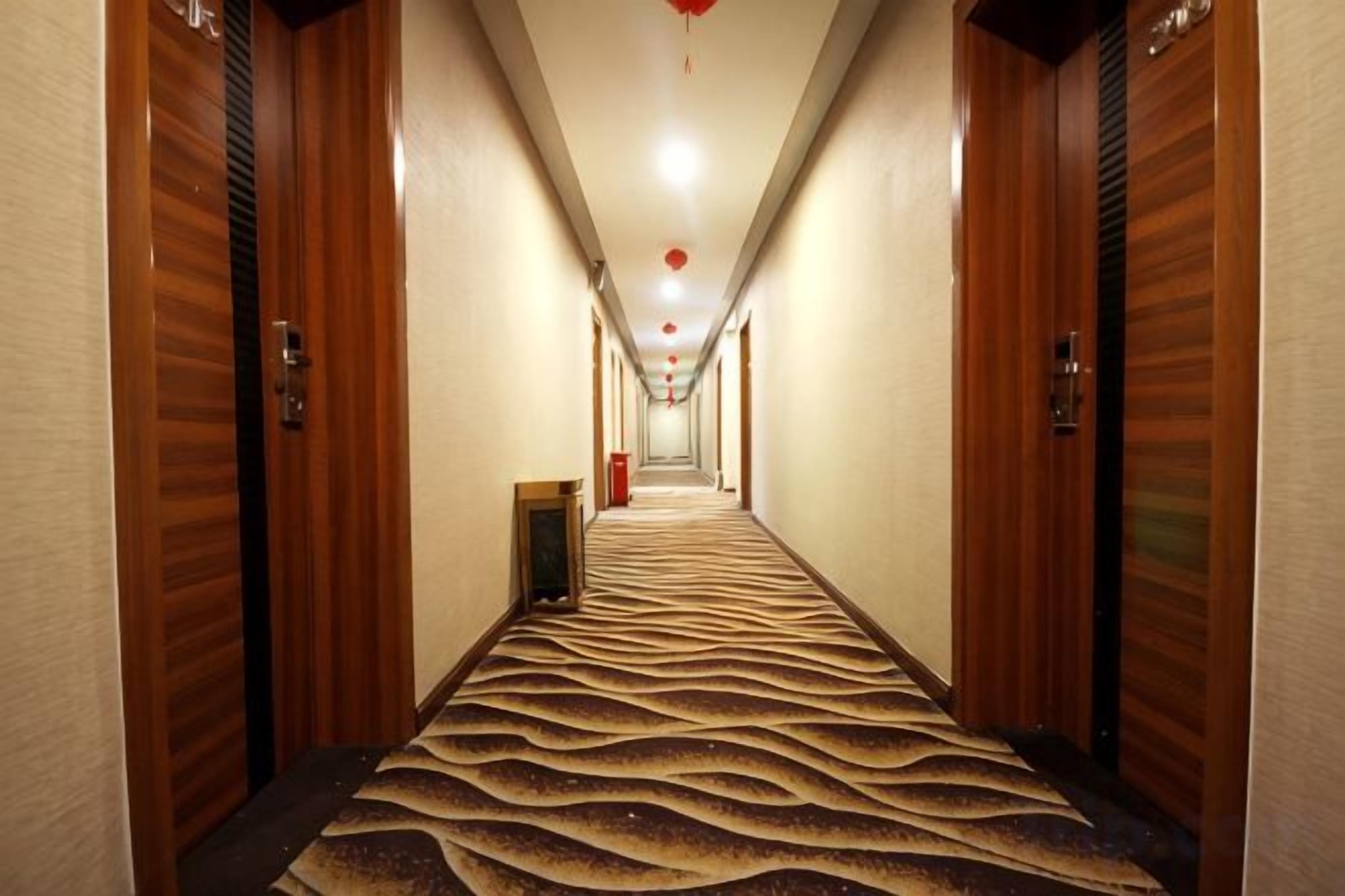Ein Hotelgang mit Holztüren, einem gemusterten Teppich und einer roten Leuchte an der Decke.