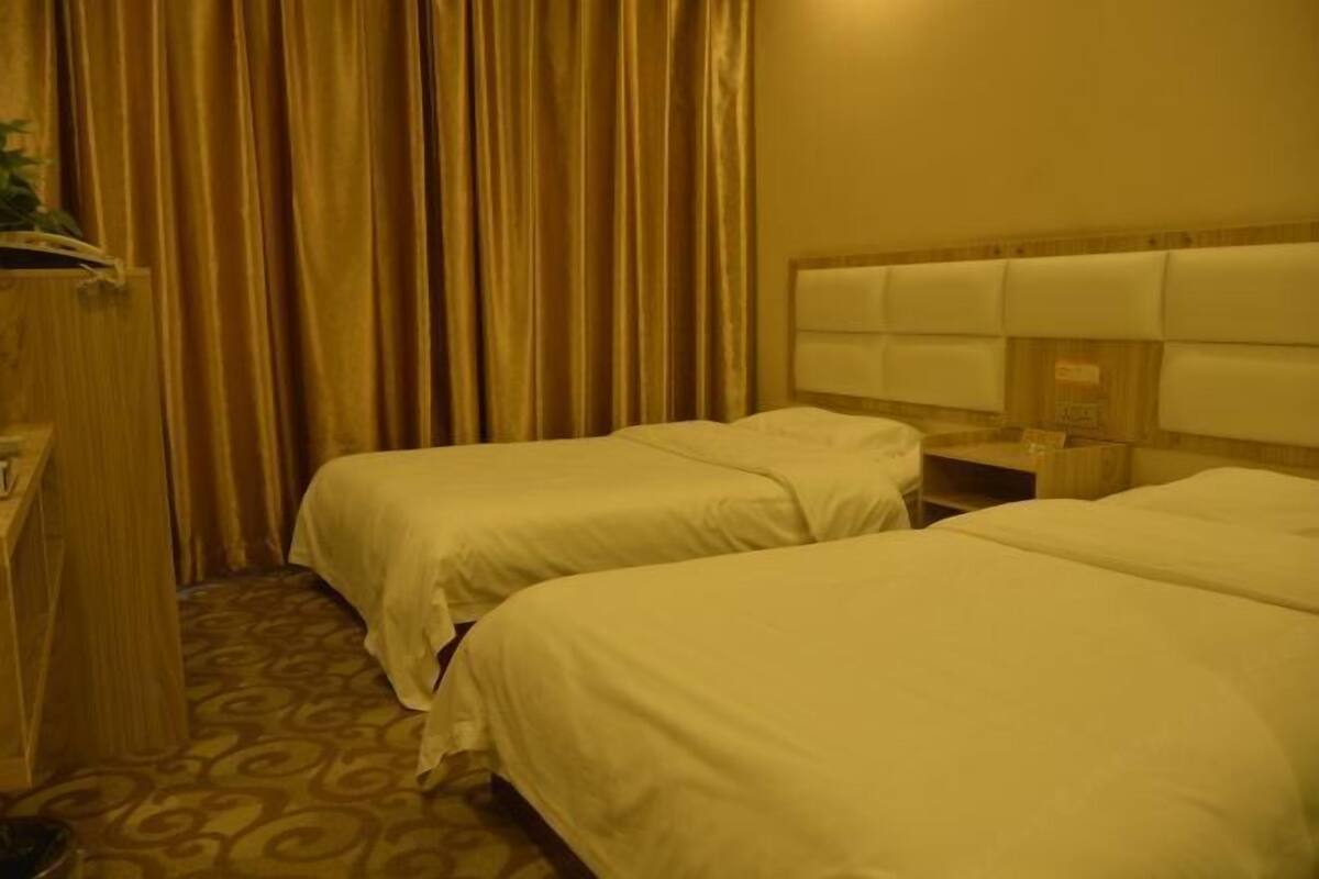 Een hotelkamer met twee bedden, een houten hoofdbord, een nachtkastje en een gordijn.