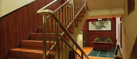 Una escalera de madera con barandillas de metal que conduce a una zona de descanso con un banco y una obra de arte enmarcada.