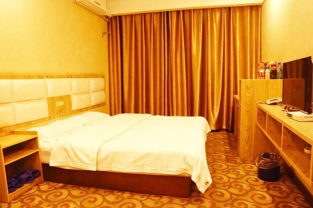 Een hotelkamer met een bed, een houten bureau, een televisie en een kledingkast.