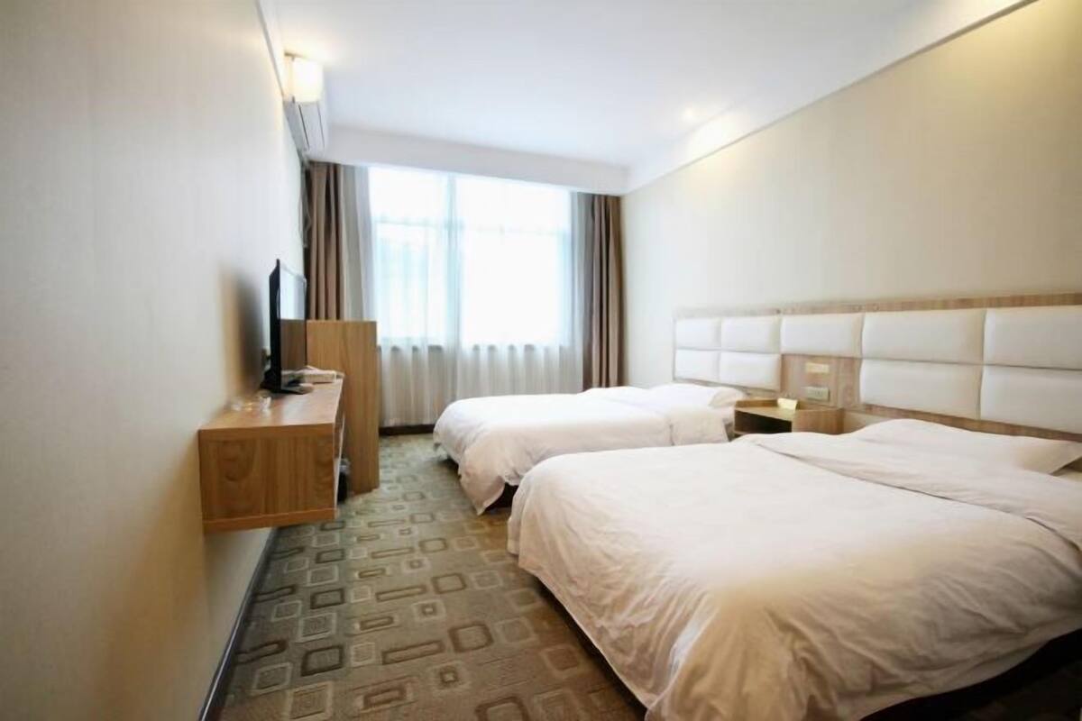 Een hotelkamer met twee bedden, een houten nachtkastje, een televisie en een raam met gordijnen.