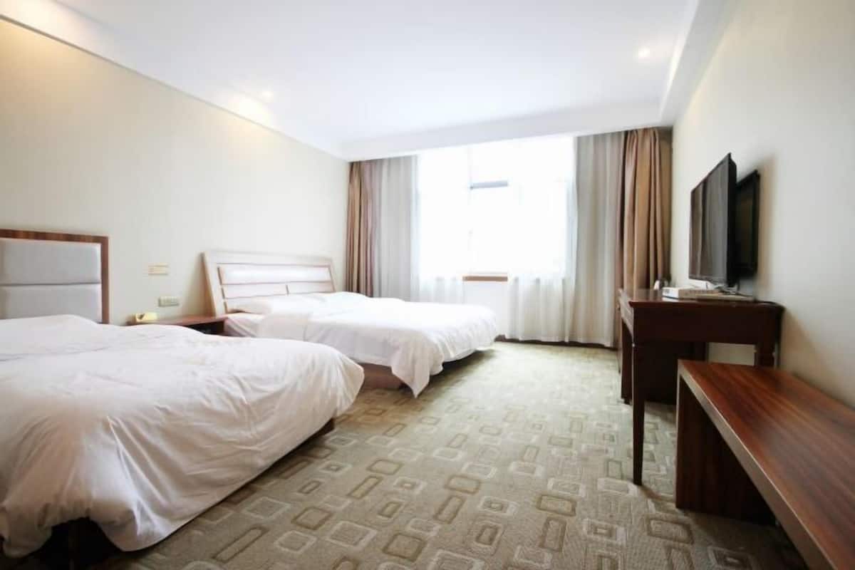 Een hotelkamer met twee bedden, een bureau, een televisie en een raam met gordijnen.