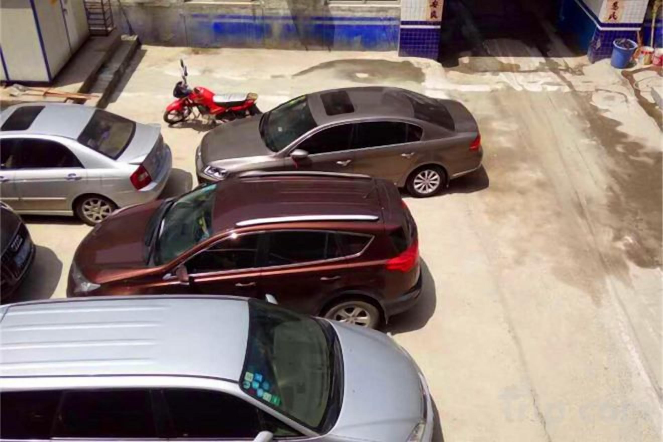 A parking area with several cars and a motorcycle.