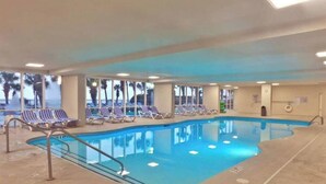 An indoor swimming pool with blue water, surrounded by lounge chairs and a concrete floor. - Pristine Oceanfront Suite with Enticing Views (Myrtle Beach)