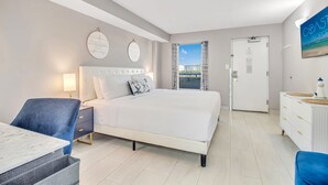 Ein Hotelzimmer mit Bett, Nachttisch, Sessel und Blick auf die Stadt durch ein Fenster.
