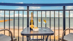 Ein Balkon mit einem Tisch für zwei Personen, ausgestattet mit einer Flasche Chandon Champagner, zwei Gläsern und einer kleinen Schale Brot. Im Hintergrund ist das Meer und ein Holzboot zu sehen.