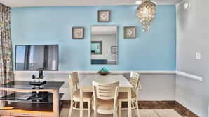 A dining area with a round table, four chairs, a TV mounted on the wall, and a chandelier. - Unforgettable Beachfront Bliss (Myrtle Beach)