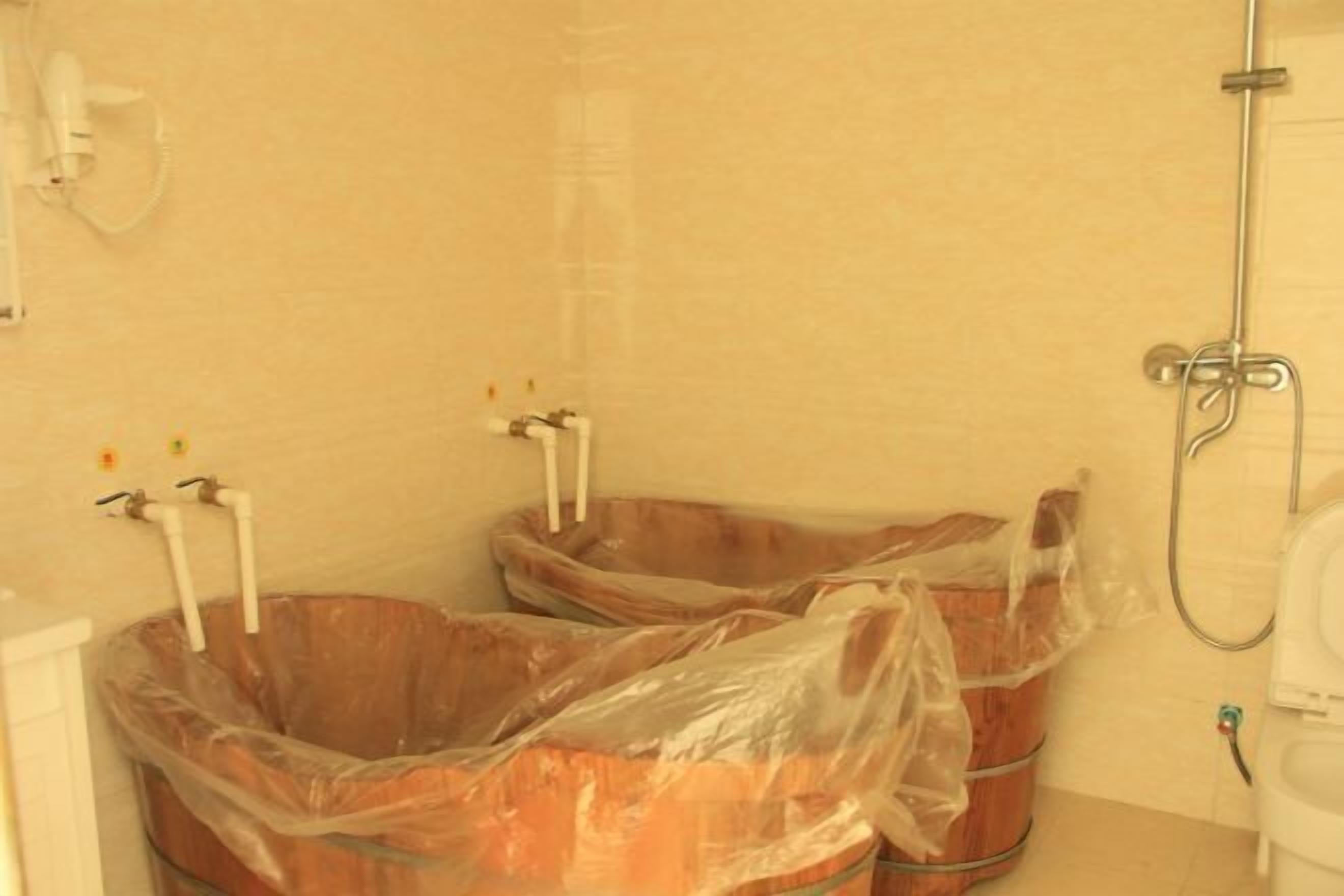 A bathroom with two large buckets, a shower, and a toilet.