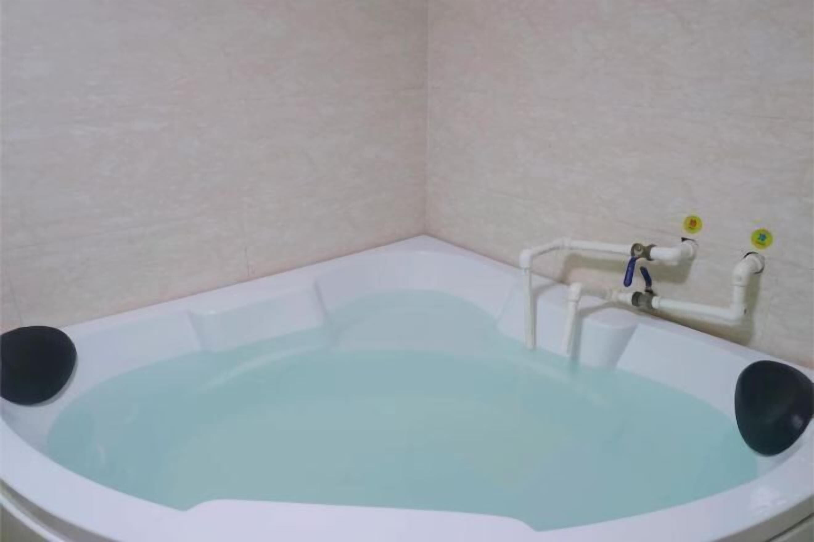 Eine Eckbadewanne mit weißem Innenraum, einem schwarzen Sitz und sichtbaren Rohren.