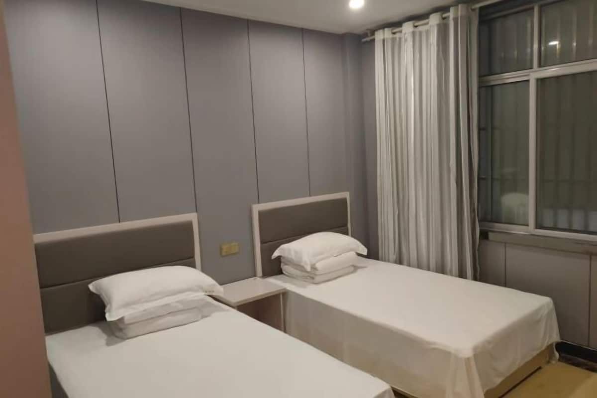 Ein Hotelzimmer mit zwei Einzelbetten, einem Vorhangfenster und einer Wand mit Wandpaneelen.