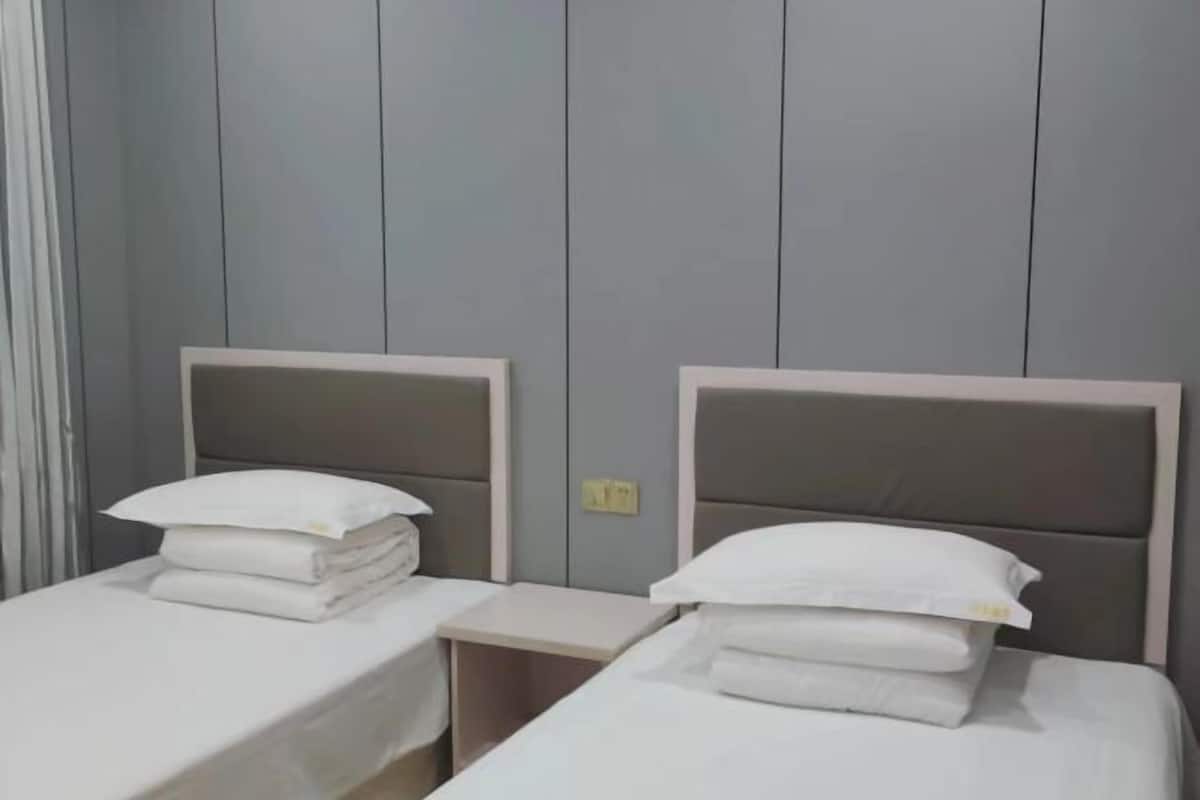Ein Hotelzimmer mit zwei Einzelbetten, jeweils mit Kopfteil und Kissen.