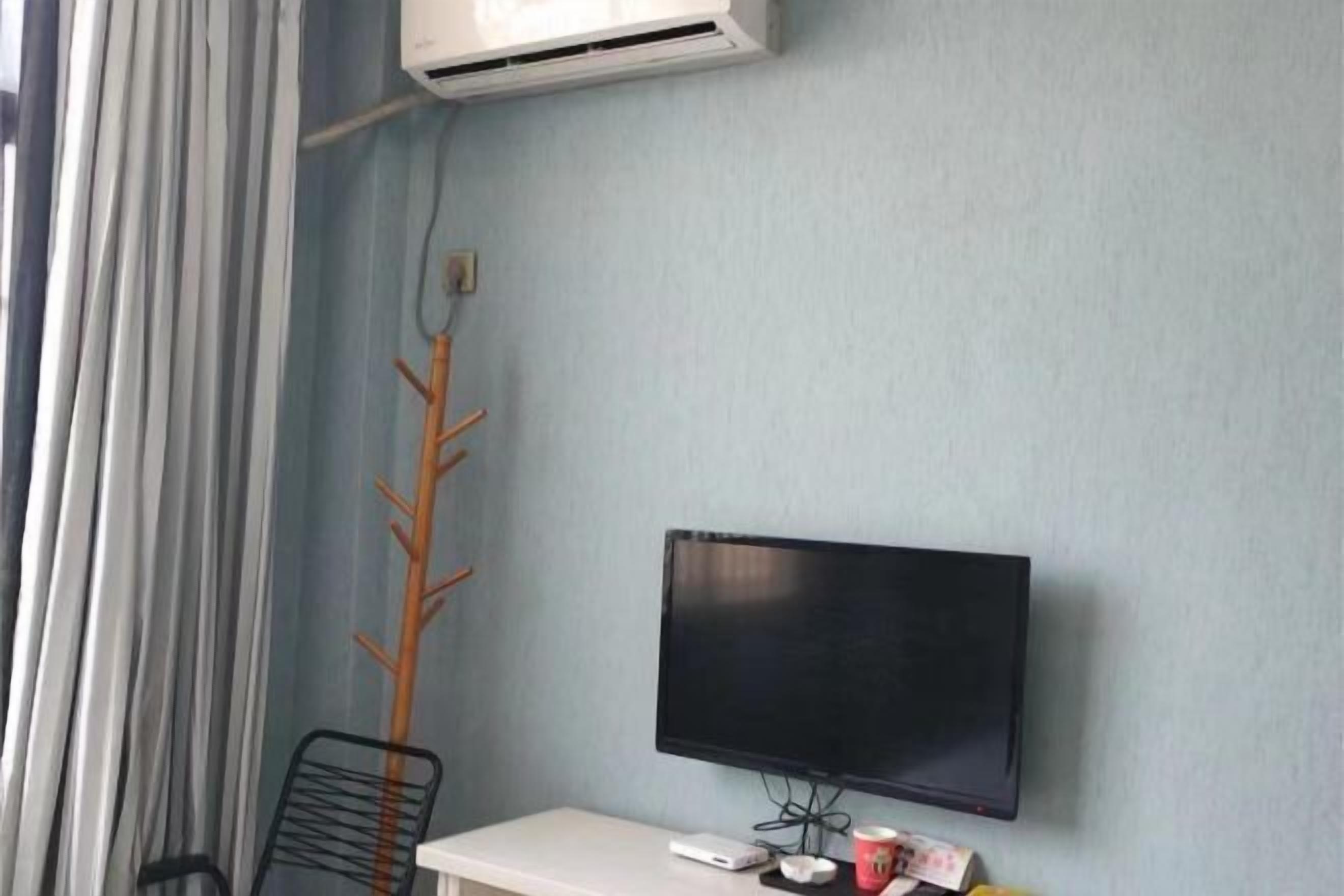 A room with a flat-screen TV mounted on the wall, a white desk, and a chair.