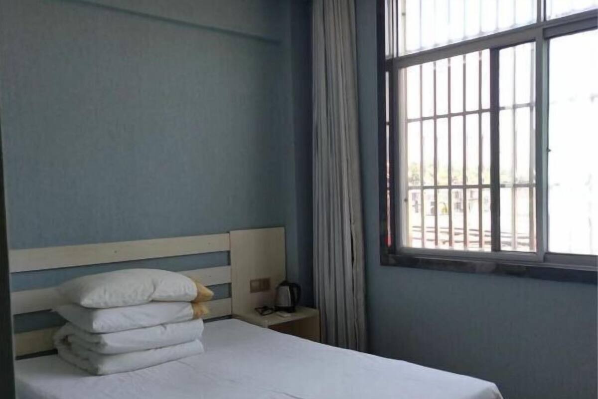 Ein Hotelzimmer mit Bett, Nachttisch, einem Fenster mit Gitterstäben und Vorhängen.