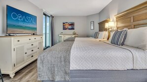 A bedroom with a large bed, a TV on a dresser, a desk, and a painting on the wall. - Escape to the Ocean~ Oceanview Suite @CompassCove (Myrtle Beach)