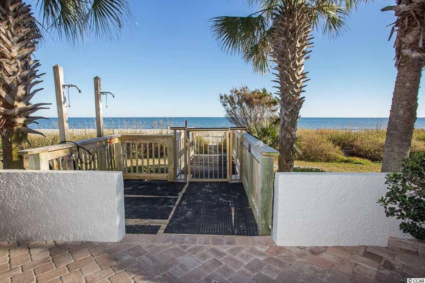 A wooden gate leading to a beach area with a clear view of the ocean.