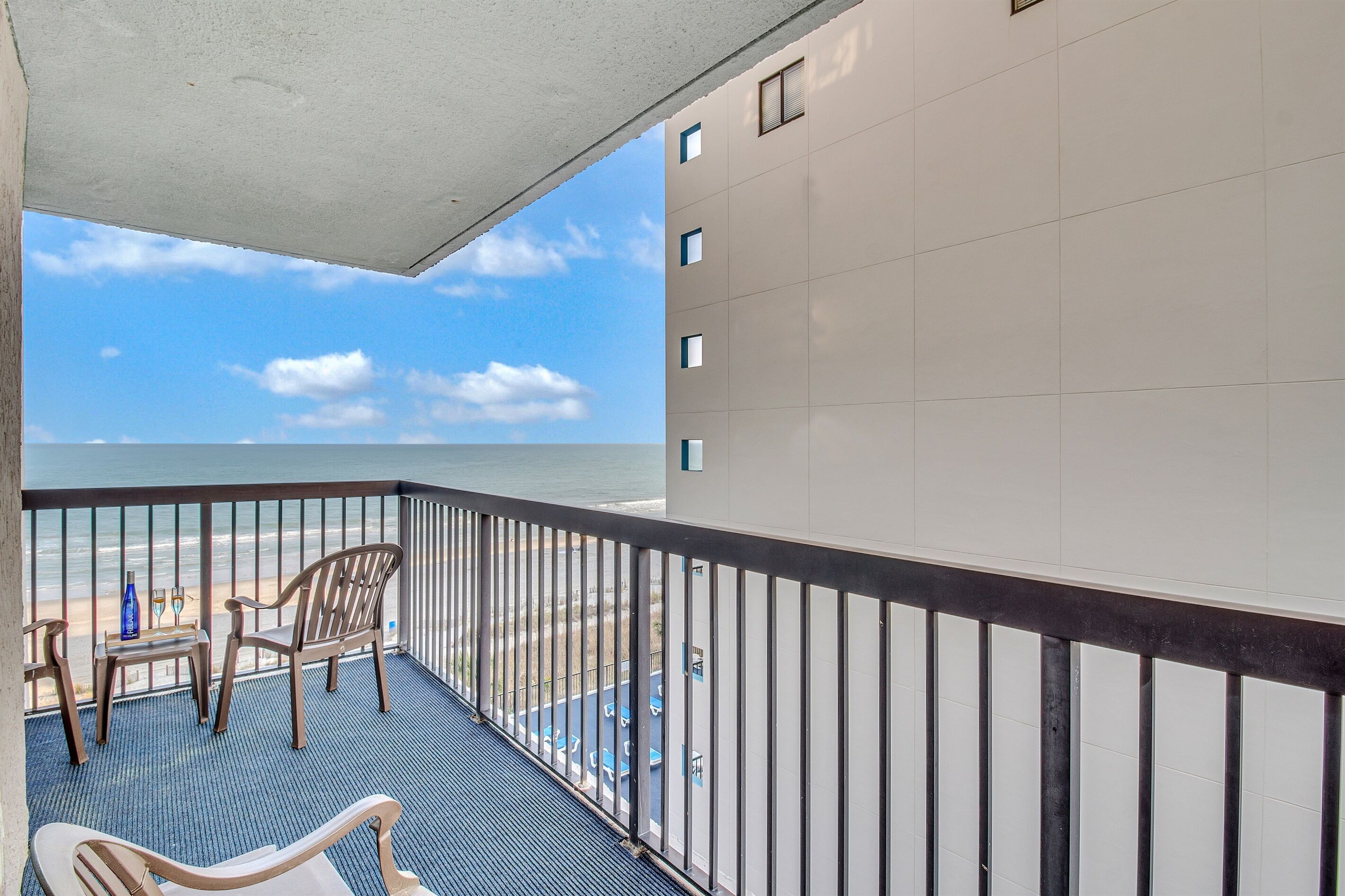 Un balcon avec vue sur la plage, une table avec des chaises et un espace piscine.