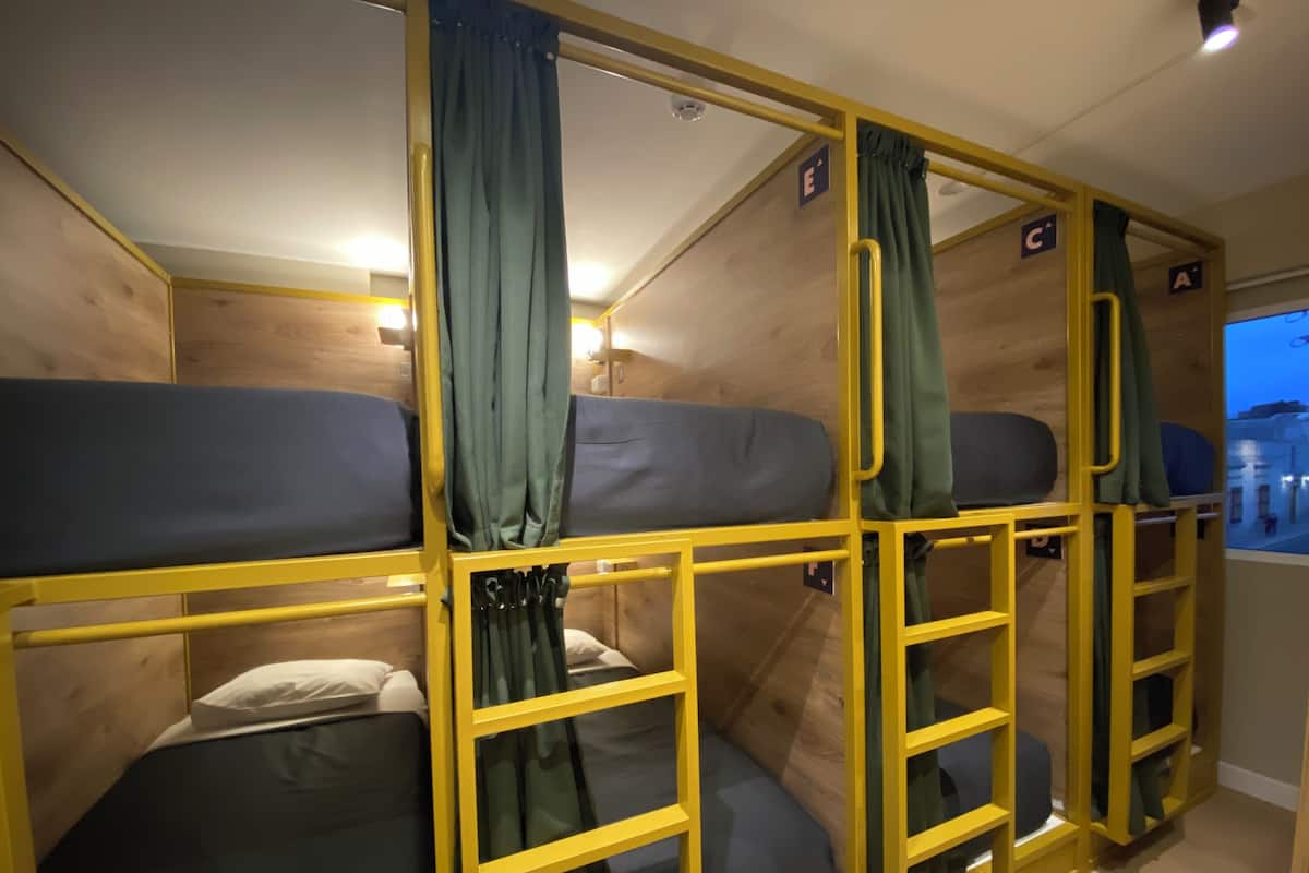 A train compartment with bunk beds, yellow metal railings, and curtains.
