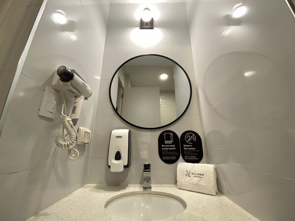 Un baño moderno con un lavamanos, un secador de pelo, un espejo y una toalla.