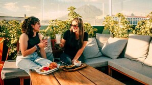 Dos personas sentadas en un sofá con una mesa delante, sosteniendo bebidas y comida.