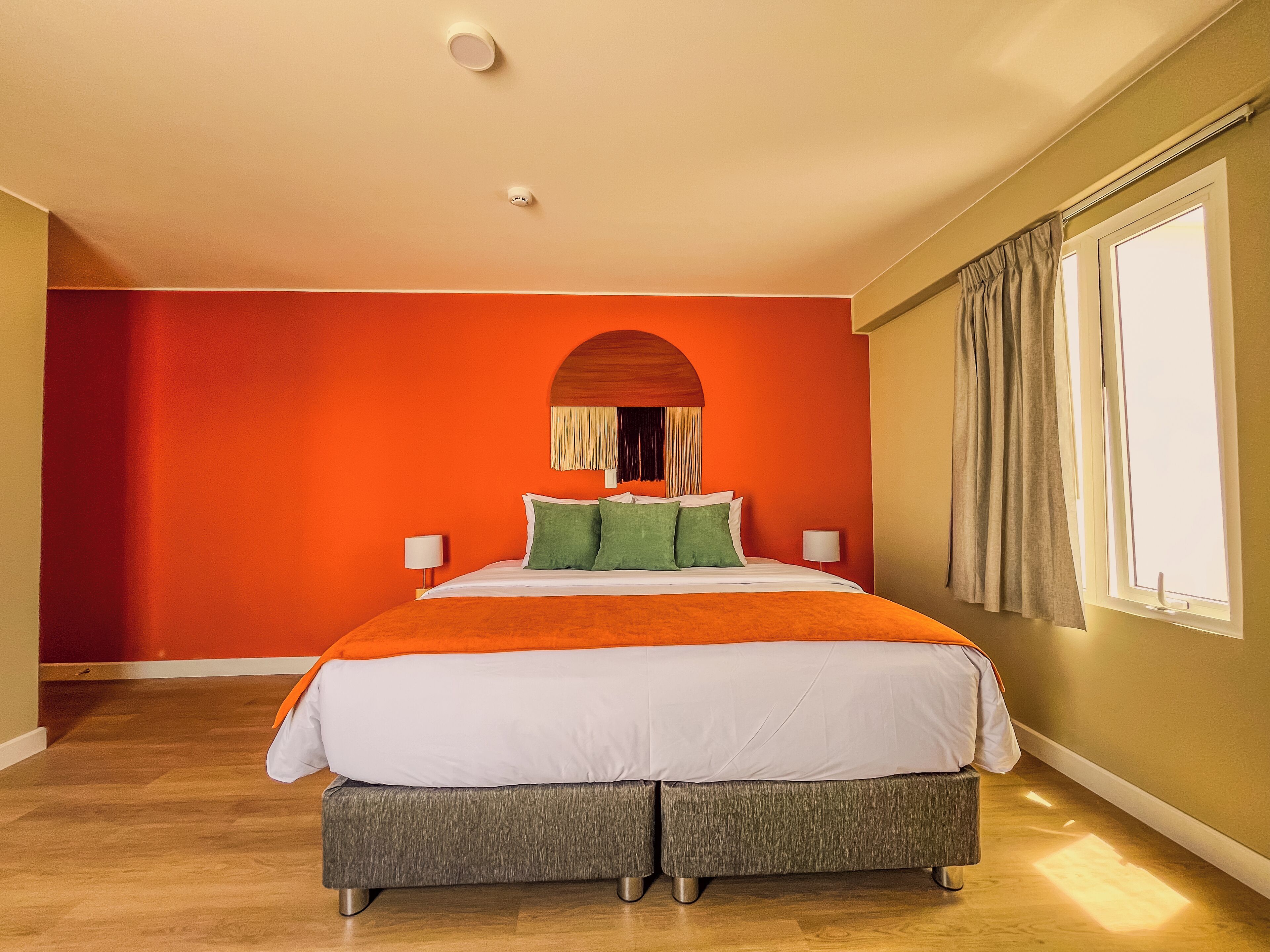 A bedroom with a large bed, two bedside tables, a window with curtains, and a ceiling light.