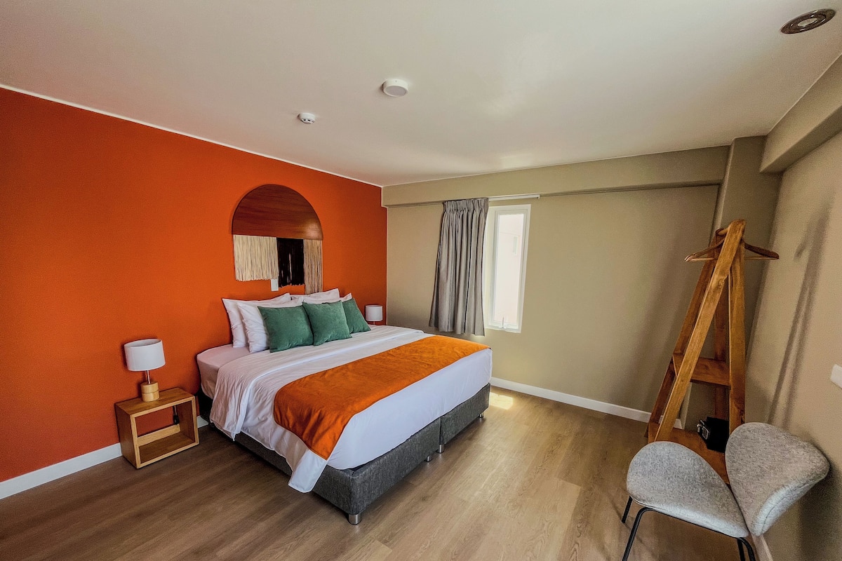 A bedroom with a bed, a nightstand, a chair, a wooden ladder, and a window with curtains.