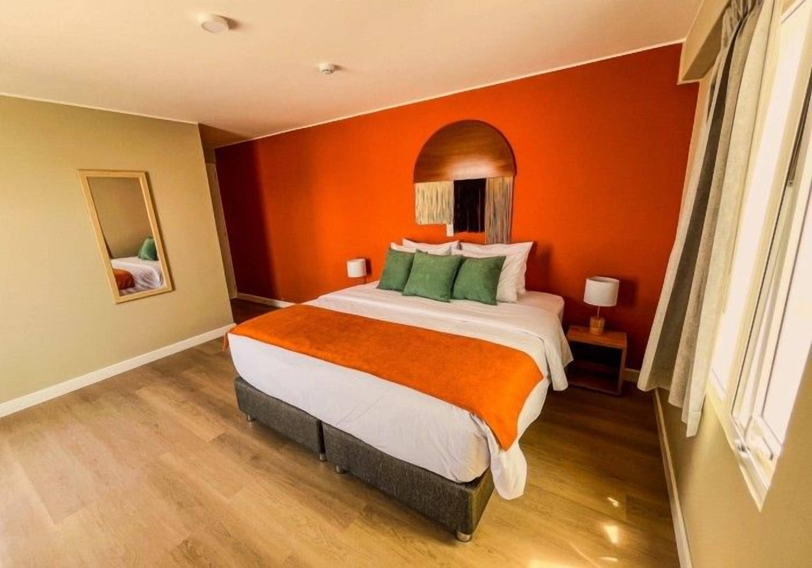 A hotel room with a large bed, a nightstand, a mirror, and a window with curtains.