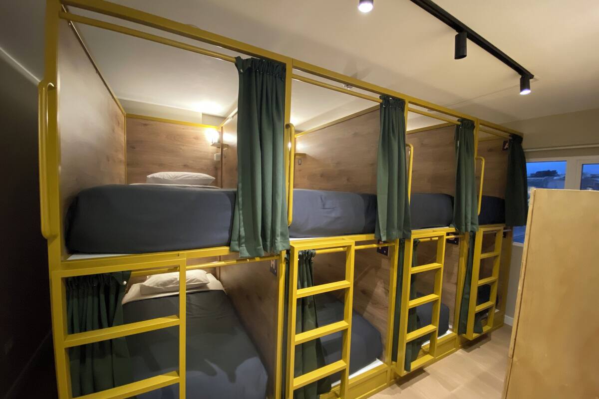 A dormitory-style room with bunk beds, wooden walls, and a window with a view.