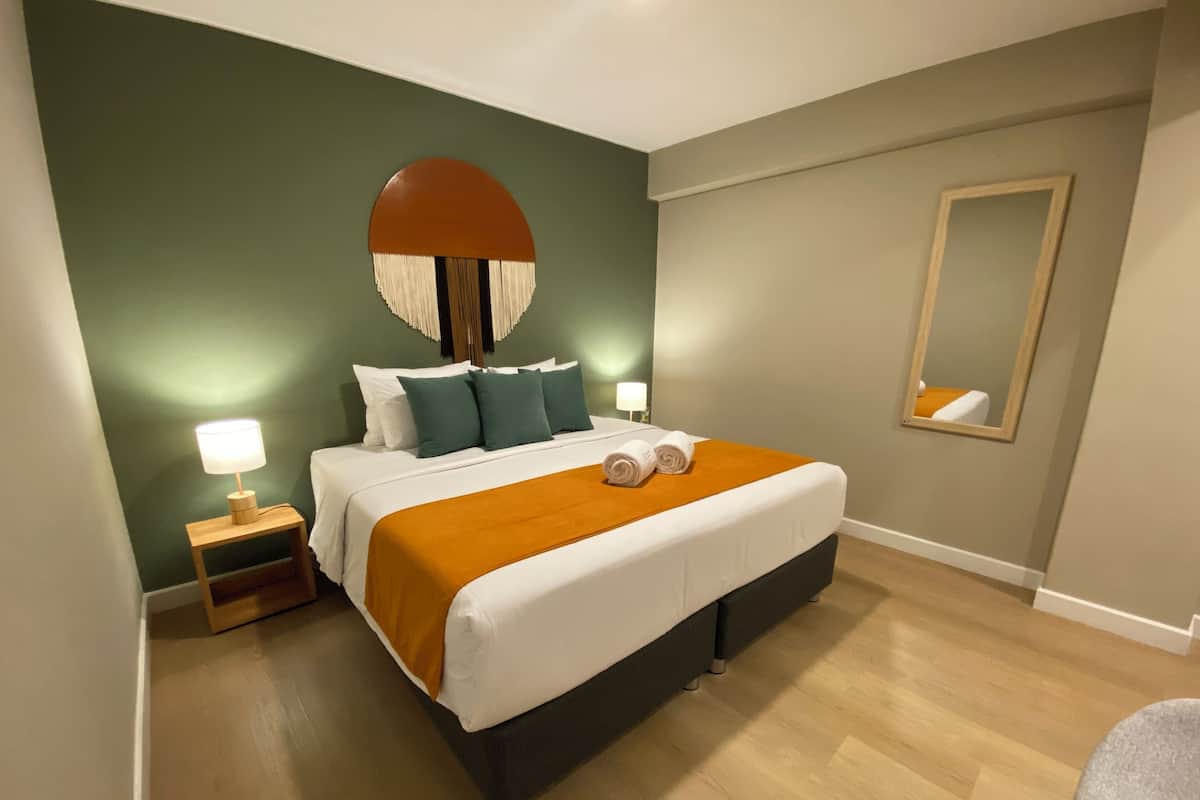 A neatly arranged bedroom with a bed, bedside lamps, a mirror, and a chair.