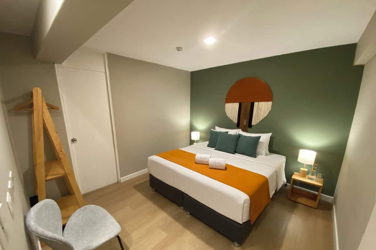 A bedroom with a bed, bedside table, lamp, chair, and a wooden ladder.