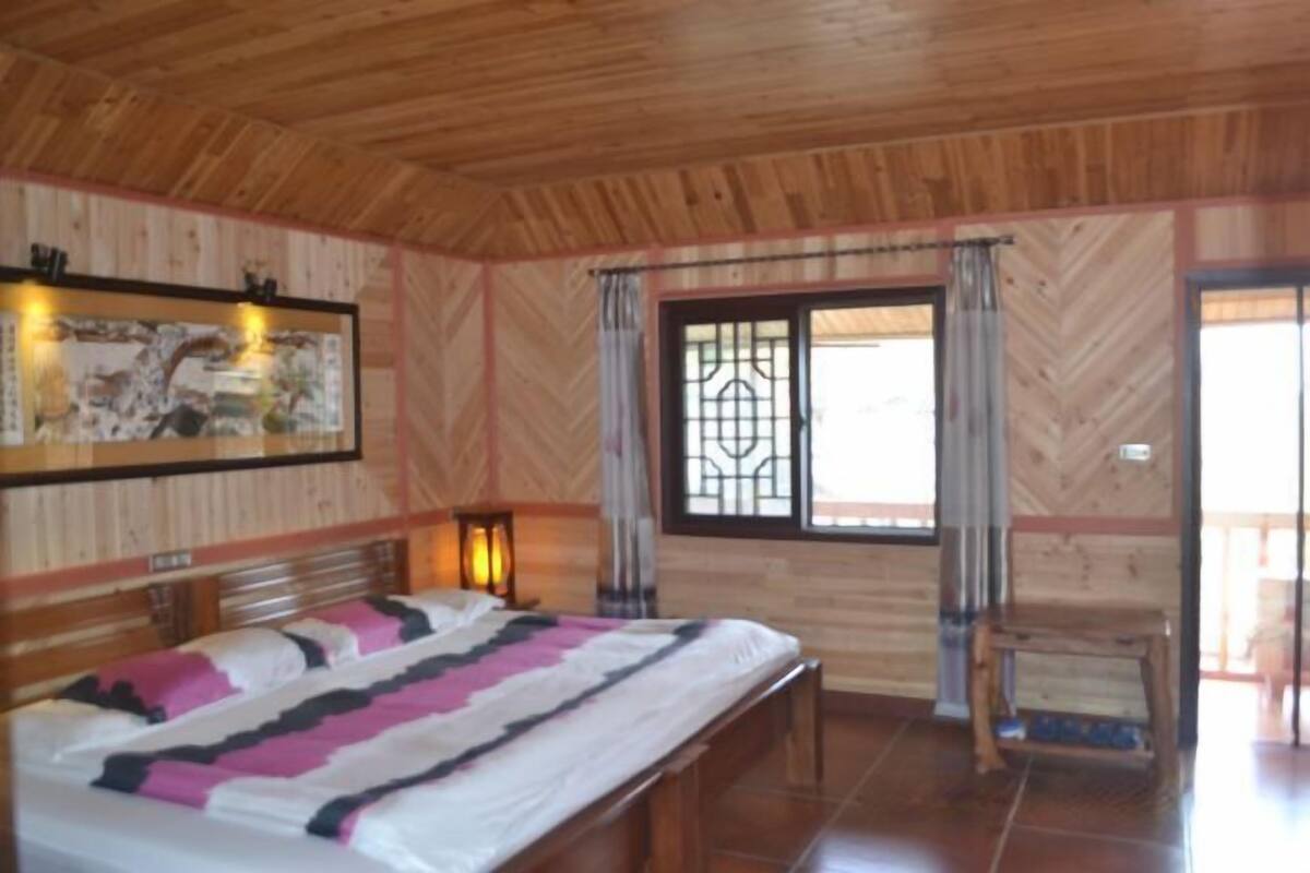 Une pièce aux murs lambrissés, comprenant un lit, une table de chevet et une fenêtre avec des rideaux.