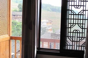 A room with a large window overlooking a rural landscape with houses and greenery. - Jiuqi · Longsheng Longji Holiday Homestay (Longsheng)