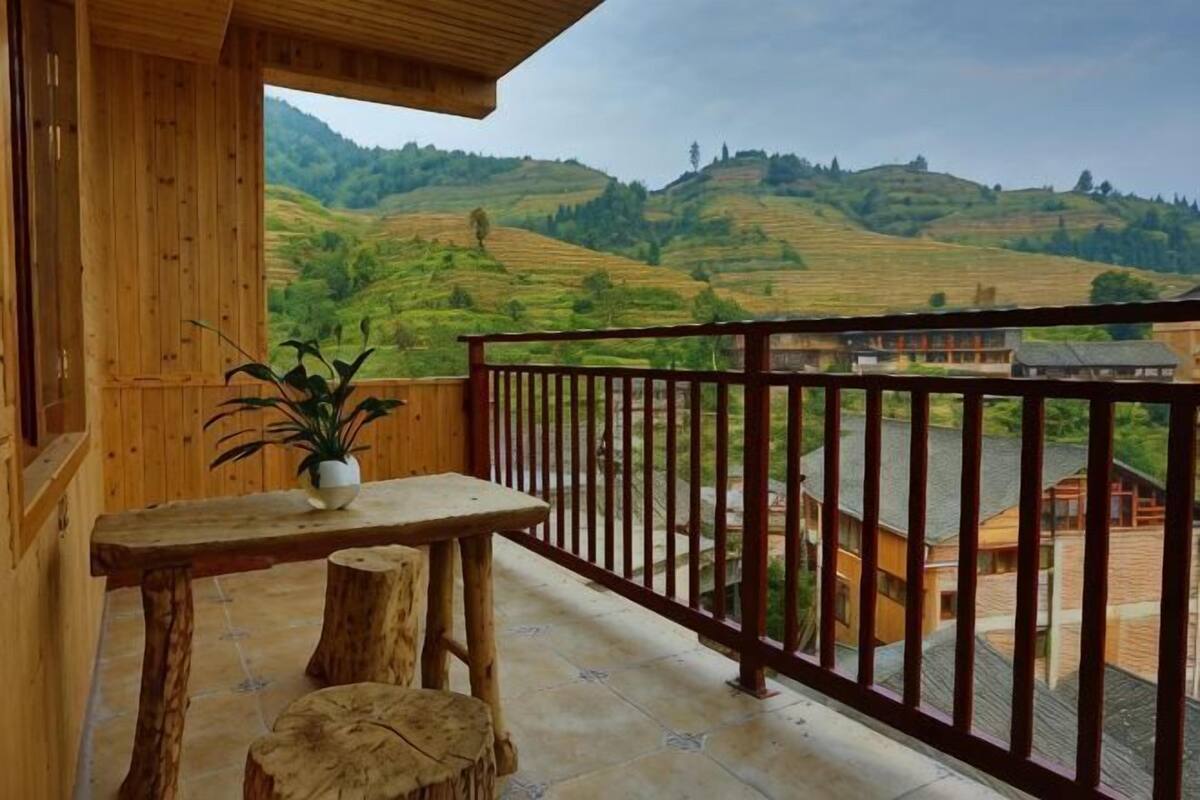 Un balcon en bois offrant une vue sur des champs en terrasses et des bâtiments.