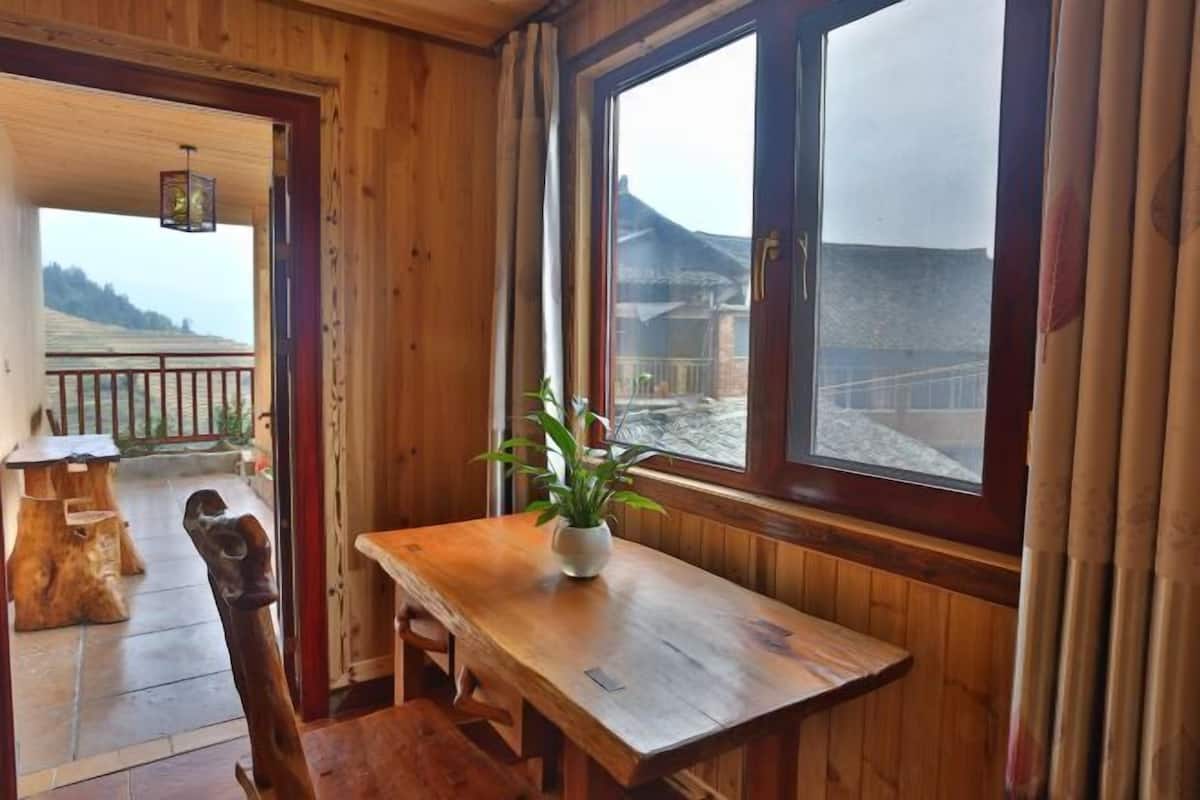 Un intérieur en bois avec une table et des chaises, une plante en pot et une vue sur un paysage enneigé par la fenêtre.