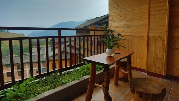 Un balcon en bois avec une table et des chaises, un pot de fleurs et une vue sur des bâtiments et des montagnes lointains.