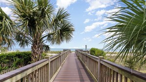 A wooden boardwalk leading to a beach with palm trees and a clear sky. - Stylish Escape Oceanview Suite @ Meridian Plaza! (Myrtle Beach)