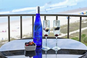Una mesa con una botella de Riesling, dos copas con bayas y un cuenco de frutos rojos en un balcón con vistas a la playa.