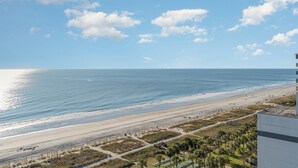A beach view with a clear sky, a sandy beach, and a building in the foreground. - Stylish Escape Oceanview Suite @ Meridian Plaza! (Myrtle Beach)