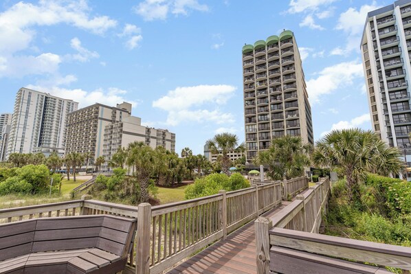 A residential area with high-rise buildings, a wooden boardwalk, and lush greenery.