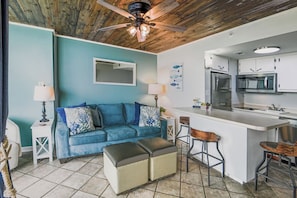 A modern kitchen with a central island, a blue sofa, and a ceiling fan. - Stylish Escape Oceanview Suite @ Meridian Plaza! (Myrtle Beach)