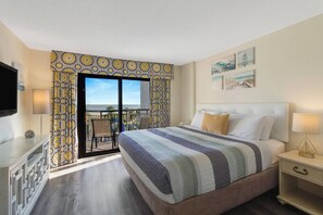 A hotel room with a bed, a TV, a balcony with patterned curtains, and artwork on the walls. - Luxurious Haven, Oceanview Suite (Myrtle Beach)
