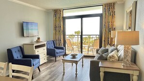 A living room with a TV, two armchairs, a sofa, a coffee table, and a balcony with outdoor furniture. - Luxurious Haven, Oceanview Suite (Myrtle Beach)