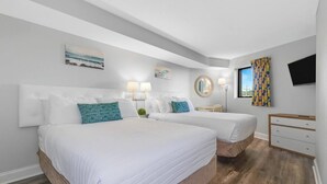 Quarto de hotel com duas camas, televisão, janela com cortinas e piso de madeira.