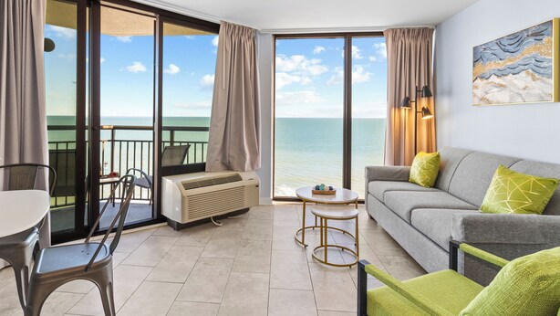 A room with a balcony, a sofa, a table, and a chair. - Remodeled Dec23/Best Floorpan/DogsOK (Myrtle Beach)