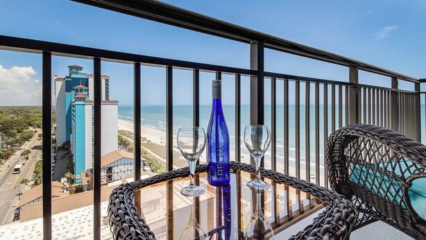 A balcony with a table set for two, overlooking a beach and a tall building.