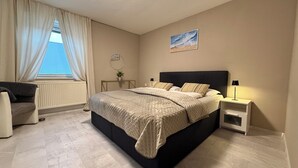 A bedroom with a bed, bedside tables, a chair, a radiator, and a window with curtains. - Townhouse Lotus in a prime location! 5 minutes from Legoland. families & pets. (Günzburg)