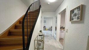 A staircase with a black railing leading to a landing. A small table with a vase and a plant is placed on the landing. The hallway is carpeted and leads to a room with a desk and chair. - Townhouse Lotus in a prime location! 5 minutes from Legoland. families & pets. (Günzburg)