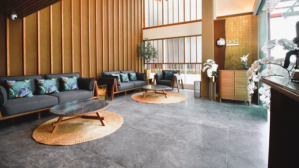 A modern lobby with a sofa, chairs, a coffee station, and a reception desk. - My Bed Gold Hotel (Chonburi)