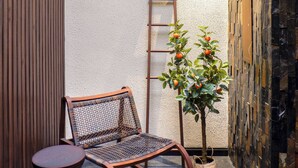 A corner seating area with a wicker chair, a small round table, and a potted plant with orange fruits. - My Bed Gold Hotel (Chonburi)