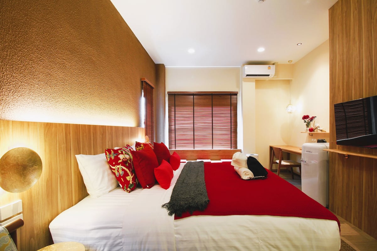 A hotel room with a bed, a desk, a chair, a TV, and an air conditioner.